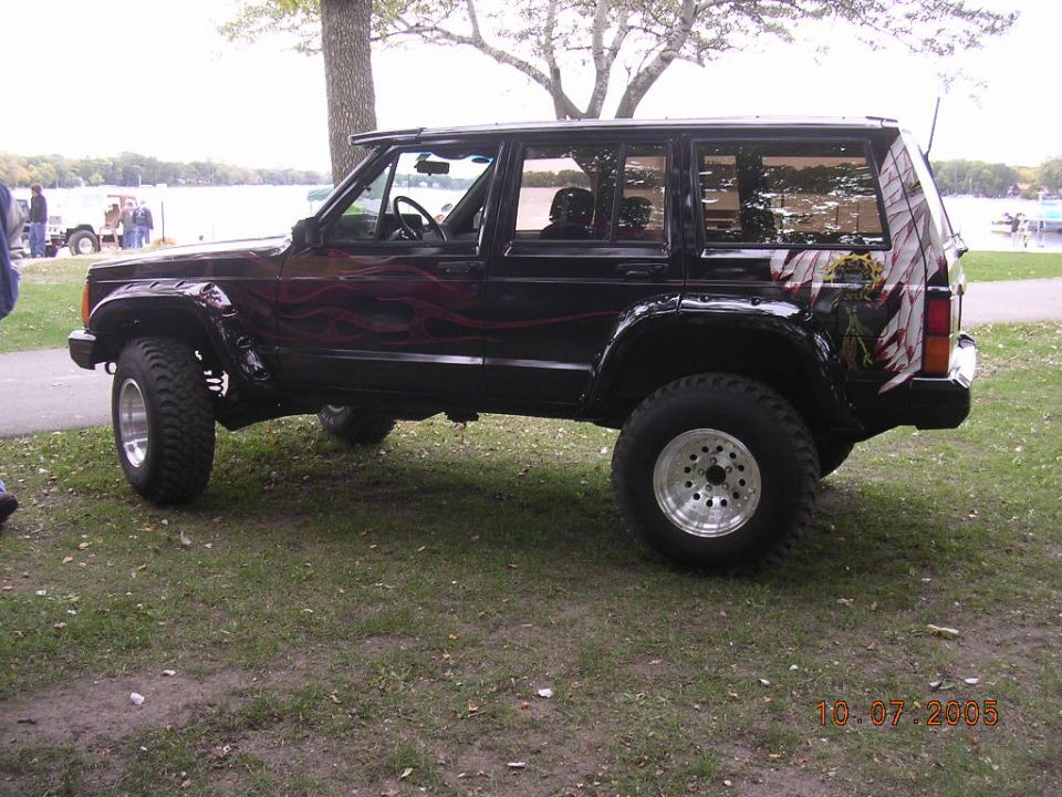 Black lifted Jeep Cherokee XJ with flame graphics by a lake