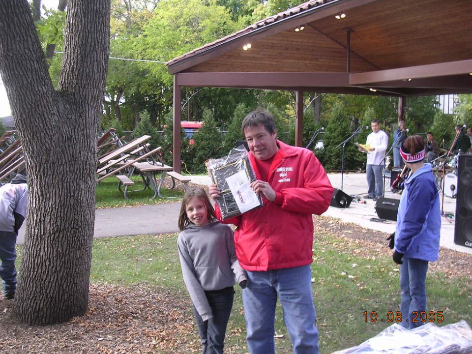 guy in red jacket holding a prize with a girl, outdoor gathering with a band playing