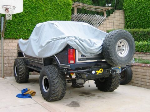 1985 Ford Bronco - This lifted 1985 Ford Bronco is partially covered, revealing its large tires and spare tire on the rear.
