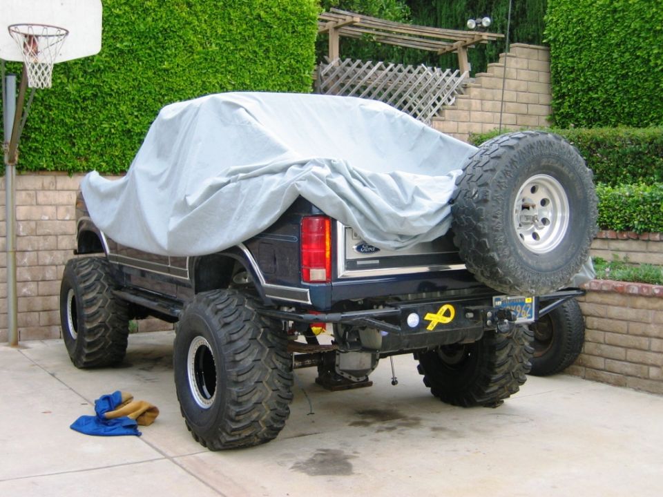 Rear of lifted dark Ford Bronco with gray cover over cab, big off-road tires and spare
