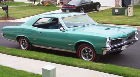 1967 Pontiac Lemans - A green 1967 Pontiac Lemans coupe is parked on the grass next to a sidewalk, with another car in the background.