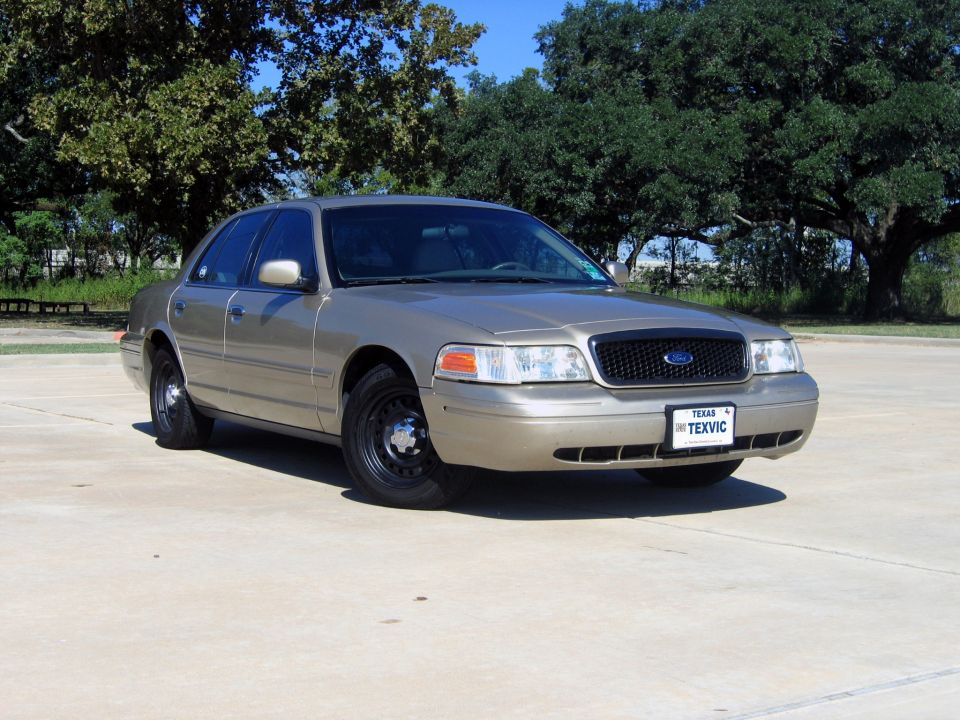 Gold Ford Crown Victoria sedan, front 3/4 view, black steel wheels, on concrete lot