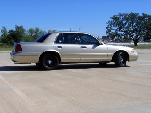 2000 Ford Crown Victoria - Side view of a gold 2000 Ford Crown Victoria with black wheels under a clear blue sky.
