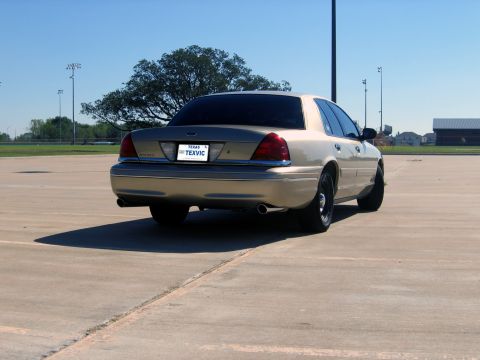 2000 Ford Crown Victoria - Rear view of a gold 2000 Ford Crown Victoria parked on a paved lot under a clear blue sky.