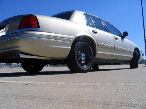 2000 Ford Crown Victoria - Rear view of a gold 2000 Ford Crown Victoria sedan with steel wheels and chrome trim under a clear blue sky.