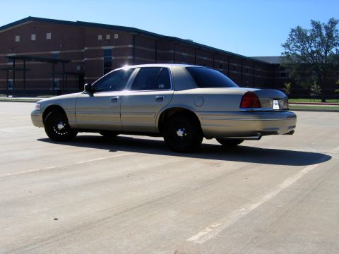 2000 Ford Crown Victoria - A tan 2000 Ford Crown Victoria is parked in an empty lot with a brick building in the background.
