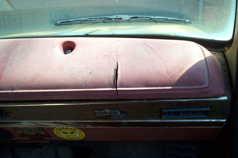 Cracked maroon dashboard with 'Trail Duster' emblem and 'Illegal Alien' sticker