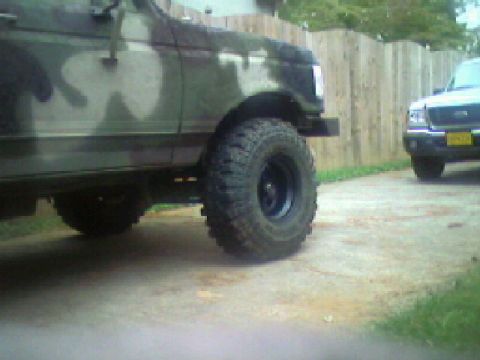 1988 Ford Bronco - A camouflaged SUV with off-road tires is parked next to another vehicle in a driveway.