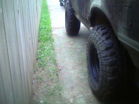 1988 Ford Bronco - A dark-colored SUV with aggressive off-road tires is seen from the side, parked closely to a wooden fence.