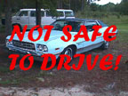 1994 Ford Crown Victoria - A light blue 1970s coupe with a "NOT SAFE TO DRIVE!" warning overlaid, parked outdoors with a van visible behind it.