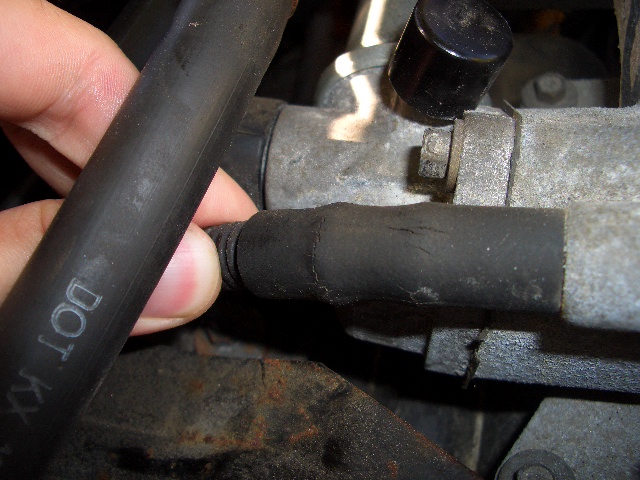 Close-up of a hand holding a cracked black hose connected to a metal engine component