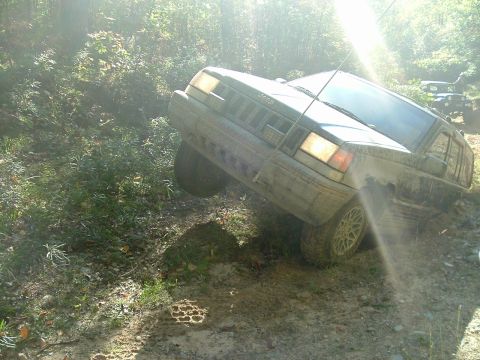 1982 Ford Bronco - A dark green Jeep Cherokee XJ navigates a steep, muddy incline with another vehicle visible in the background.