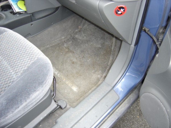 Car interior showing a blue door, grey carpet, and a grey fabric seat. A "no smoking" sticker is visible on the dashboard