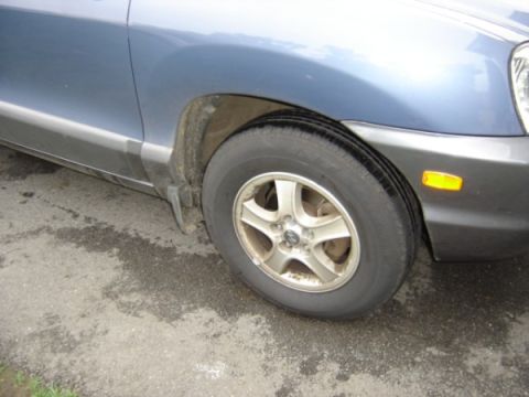1999 Ford Taurus - Close-up of the front wheel and fender area of a blue SUV, showing the tire and alloy rim.
