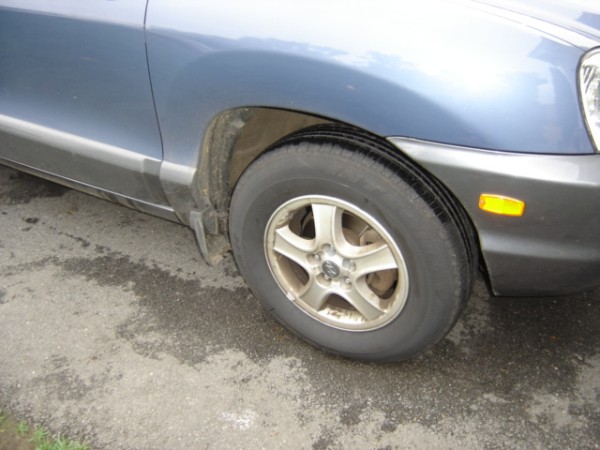 Front wheel and fender of a blue Hyundai Santa Fe, likely from the early 2000s