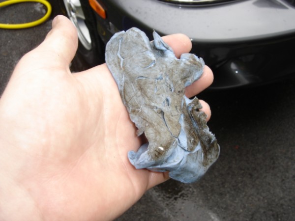 Hand holding a dirty blue clay bar with a black car in the background