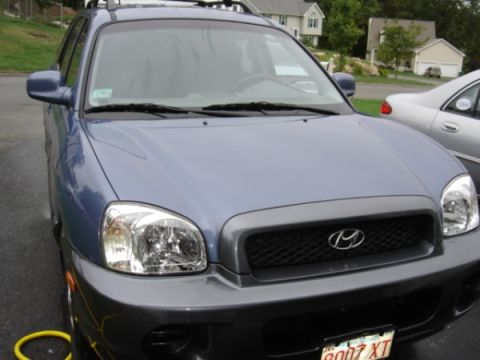 1999 Ford Taurus - A blue Hyundai Santa Fe SUV is parked in a driveway, with a silver sedan visible to its right.