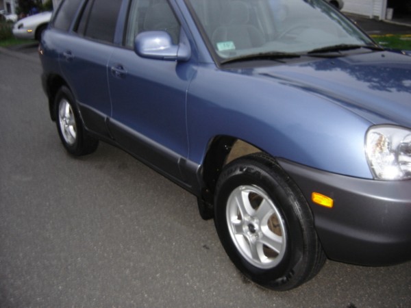 Blue SUV, 3/4 front view. Another white car is visible in the background