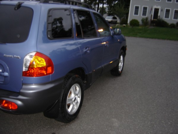 Rear quarter view of a blue Hyundai Santa Fe parked on a street. The vehicle has tinted windows and a roof rack