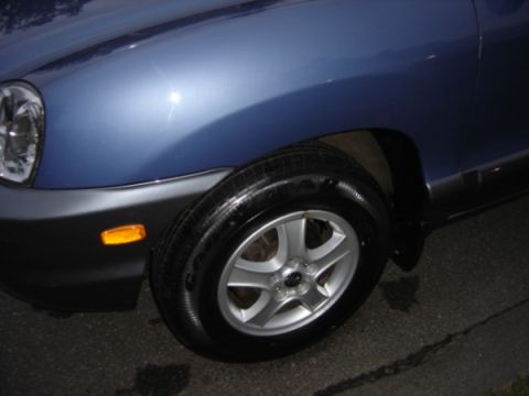 1999 Ford Taurus - Close-up of a blue SUV's front fender and wheel, showing the black lower trim and amber turn signal indicator.