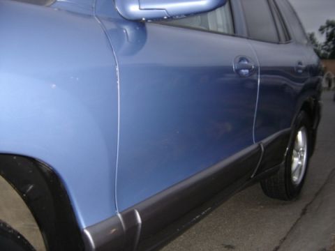 1999 Ford Taurus - Close-up of the side panel and wheel well of a blue SUV.
