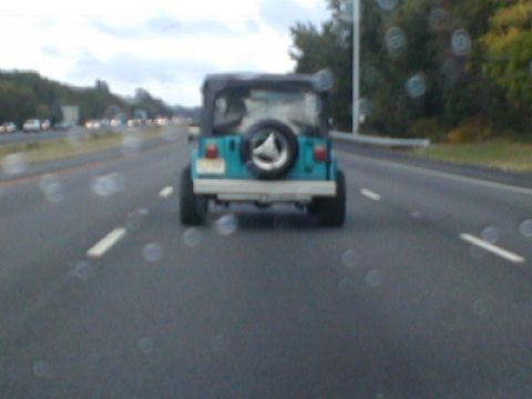1979 Ford Bronco - A teal Jeep Wrangler is seen driving on the highway from behind, with a spare tire mounted on the tailgate.