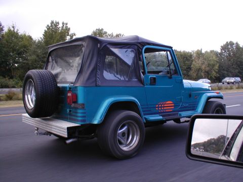 1979 Ford Bronco - Teal Jeep Wrangler YJ with soft top and spare tire on rear bumper is seen from the side while driving.