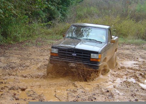 1989 Ford Ranger - A black pickup truck navigates a muddy terrain, kicking up dirt and water as it goes.