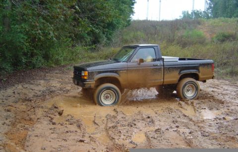 1989 Ford Ranger - A black 1989 Ford Ranger navigates a muddy terrain, with its tires deep in the mire.