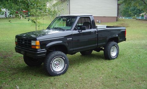 1989 Ford Ranger - This lifted black Ford Ranger pickup truck is parked on a grassy lawn in front of a residential building.