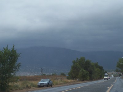 1972 Ford Ranchero - A car is parked on the side of a wet road under a cloudy sky with mountains in the distance.