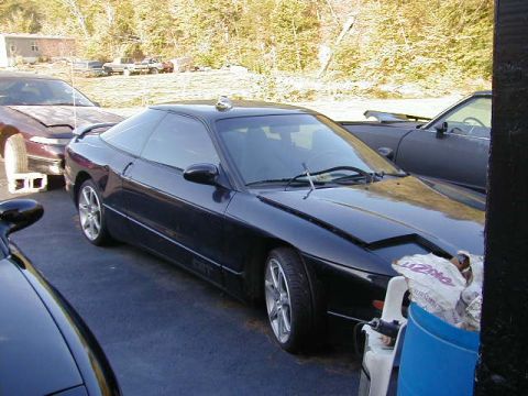 1994 Ford Probe - A black 1994 Ford Probe is parked next to other vehicles, with a blue trash can in the foreground.