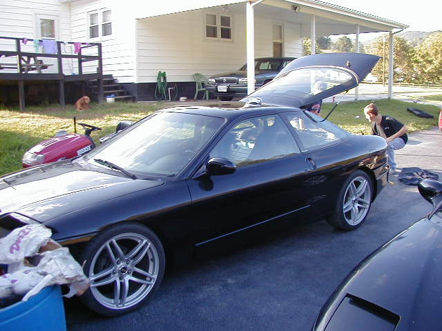 Black 1994 Ford Probe with trunk open, parked on driveway. Another car is partially visible in the foreground
