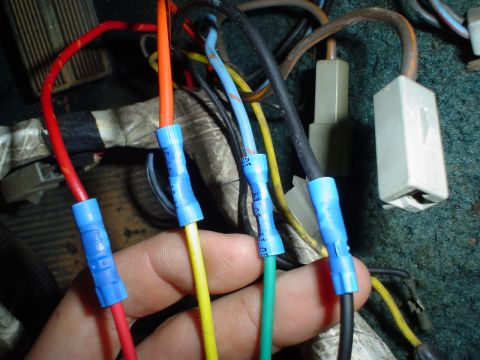1984 Ford Bronco - Close-up of a hand connecting wires within a vehicle's interior wiring harness.
