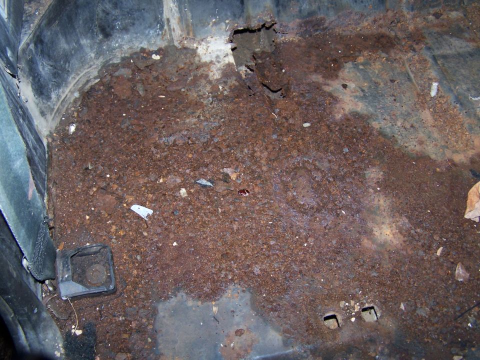 Rusted interior floor with debris and a black plastic trim piece