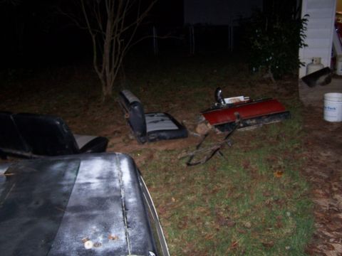 1979 Ford F-150 - Disassembled car parts, including seats and a tailgate, are scattered on the lawn in the dark.