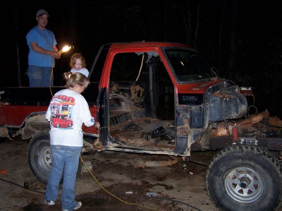 people working on a stripped-down red and black pickup truck at night