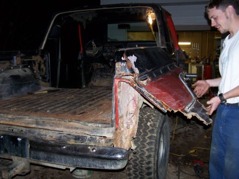 1979 Ford F-150 - A man inspects the severe rust damage on the rear quarter panel of a pickup truck.