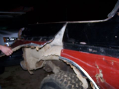 1979 Ford F-150 - The fender of a red and black truck shows significant rust and damage, with body panels missing.