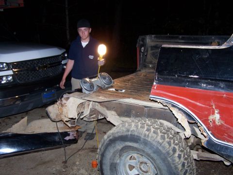 1979 Ford F-150 - A man holds a work light near the damaged bed of a red and black pickup truck.