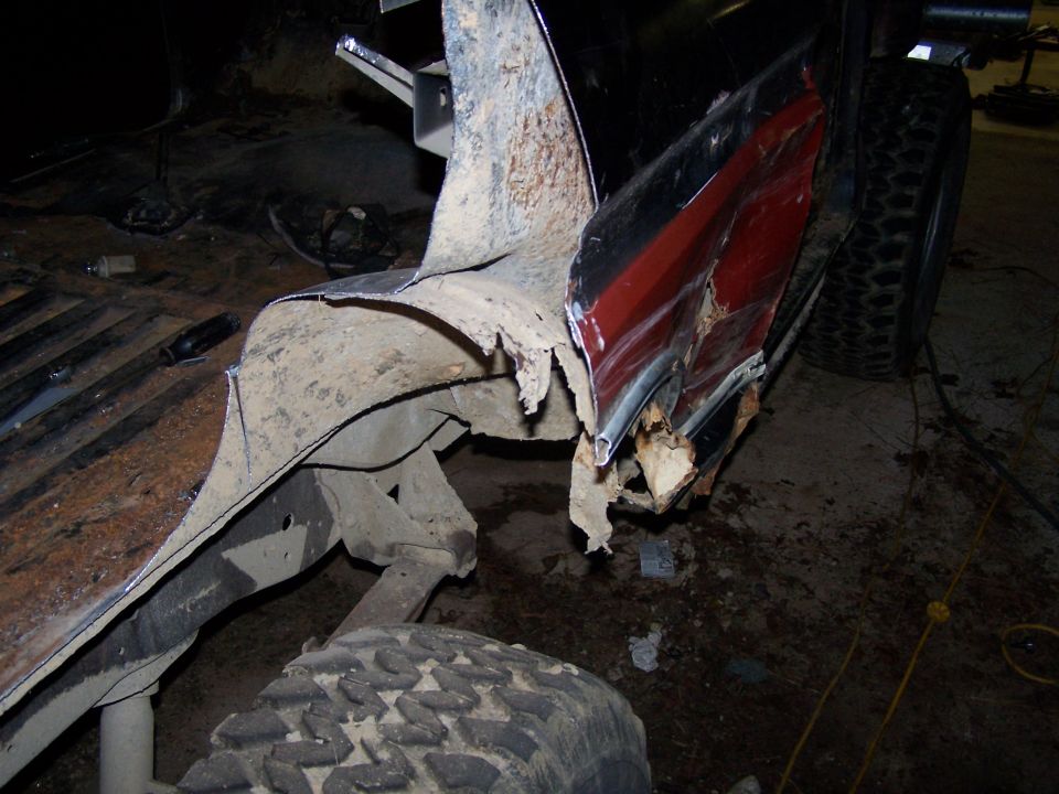 Heavily rusted and damaged rear quarter panel and fender of a truck, showing exposed metal and red paint