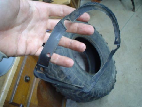 1984 Ford Bronco - A hand holds a damaged metal trim piece over a tire.