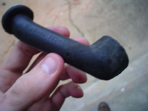 1984 Ford Bronco - A hand holds a black rubber hose part with embossed text, likely a vehicle component.