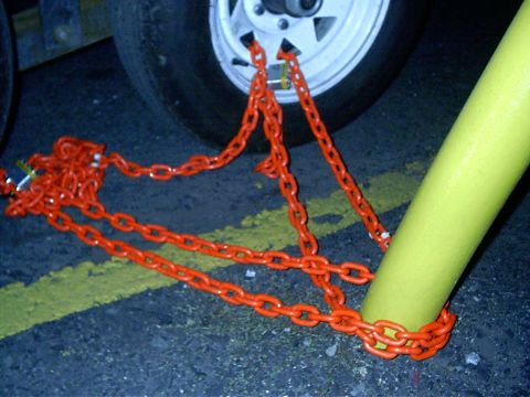 1979 Ford Bronco - Orange chains are wrapped around a trailer wheel and a yellow pole, securing it to the ground.