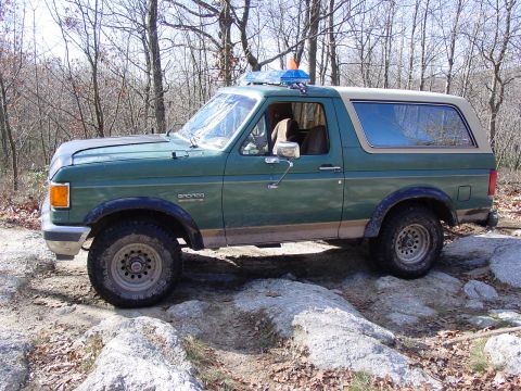 1989 Ford Bronco - A green Ford Bronco with a tan top navigates a rocky trail.