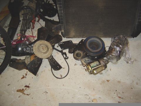 1986 Ford Bronco - Various automotive parts, including a radiator and fan, are displayed on a floor.
