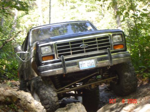 1986 Ford Bronco - Ford Bronco tackling a challenging off-road course with large rocks and trees.