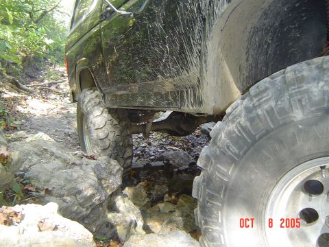 1986 Ford Bronco - A black off-road vehicle navigates a challenging rocky trail, with large tires visible.