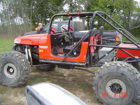 1986 Ford Bronco - An orange off-road vehicle with a roll cage sits beside a black pickup truck in a grassy area.