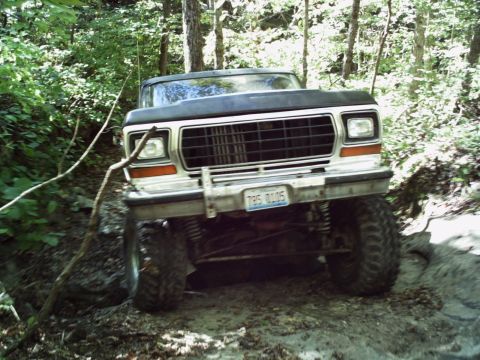 1986 Ford Bronco - This lifted Ford Bronco navigates a muddy, wooded path with its front end angled towards the camera.